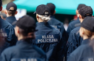 Uczniowie klasy policyjnej stojący tyłem w czapkach na głowie. Na mundurach napis Klasa Policyjna